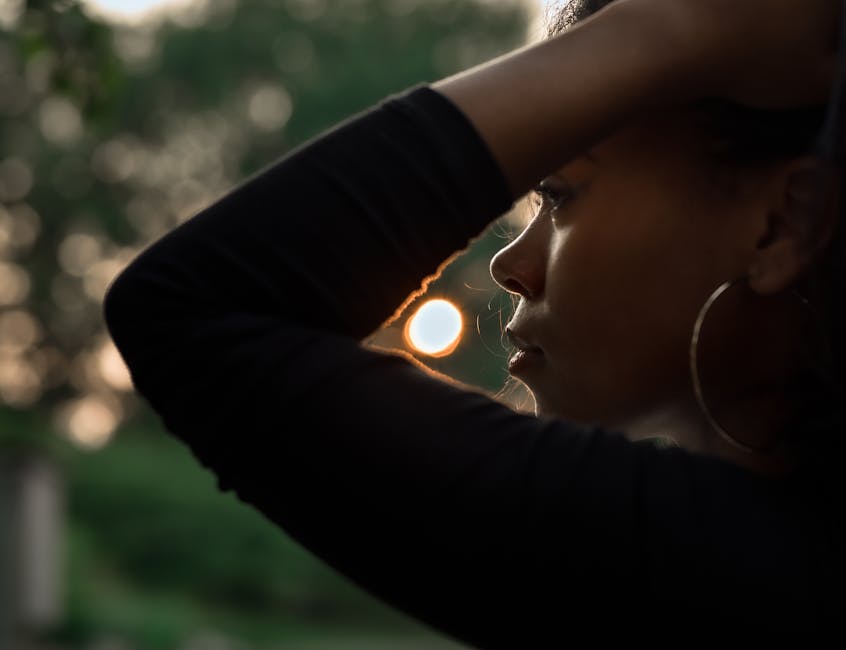 Silhouette of a woman with hoop earrings looking at the sunset, in a thoughtful pose.