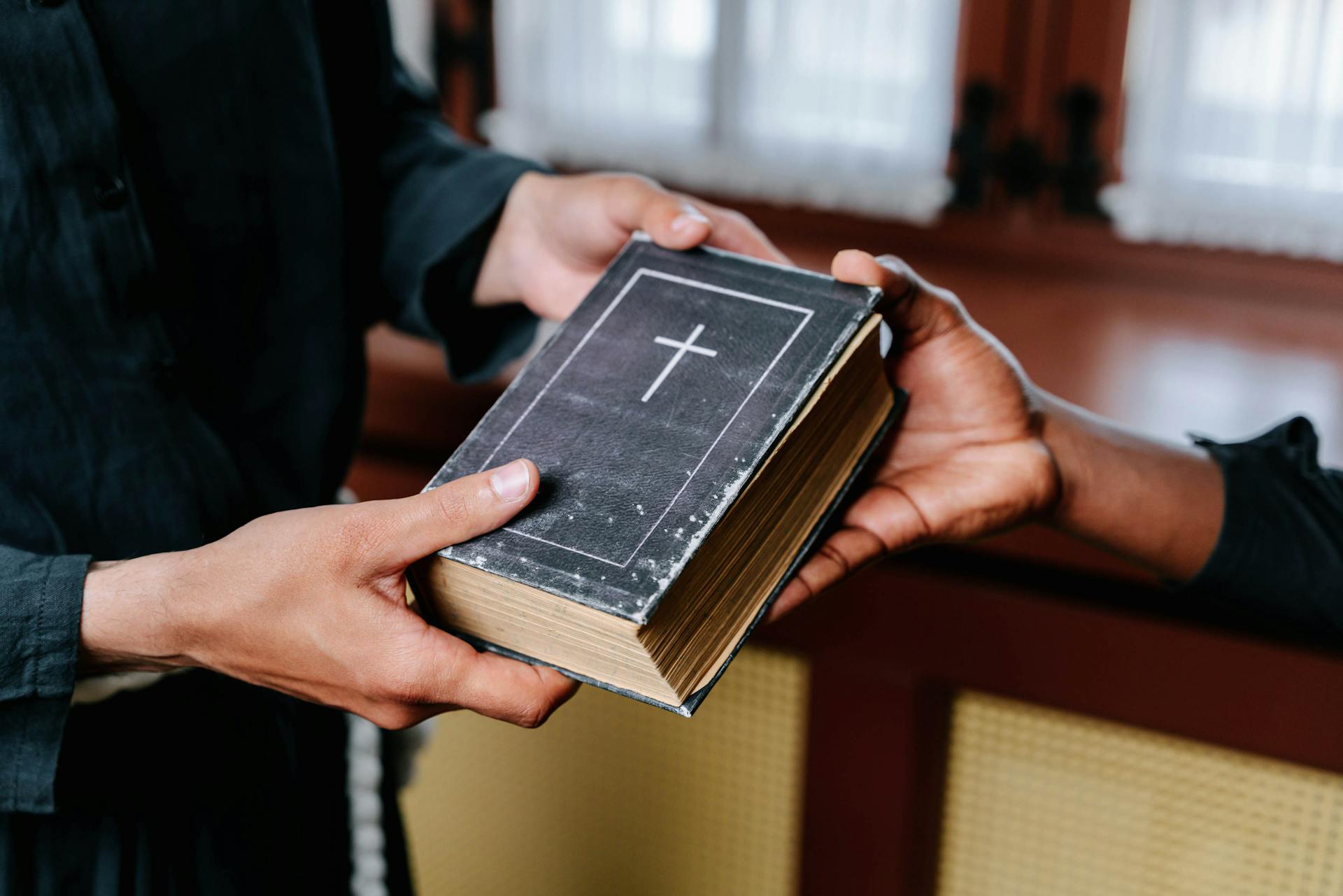 Close-up of hands exchanging a Bible, symbolizing religious connection and faith.