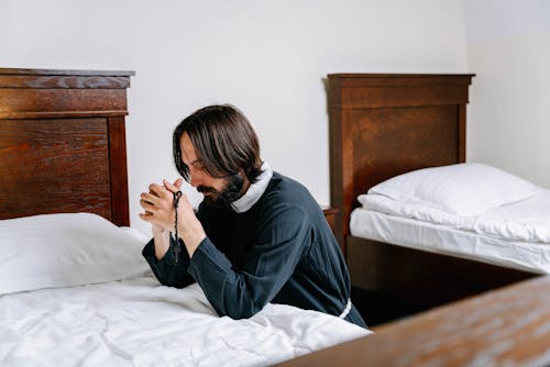 Free Man Kneeling Beside a Bed Stock Photo