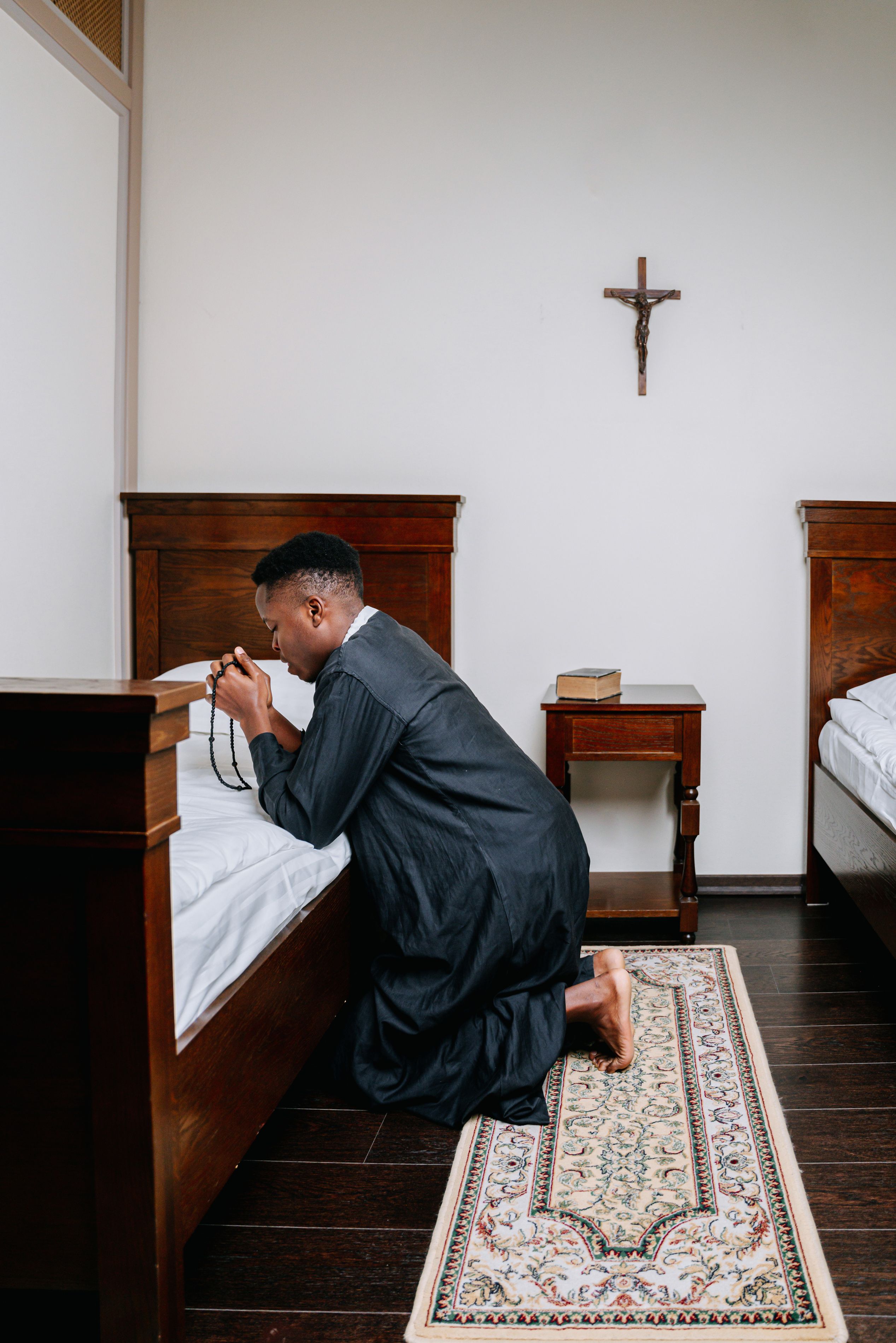A young man kneels in prayer in a room, expressing devotion and faith.