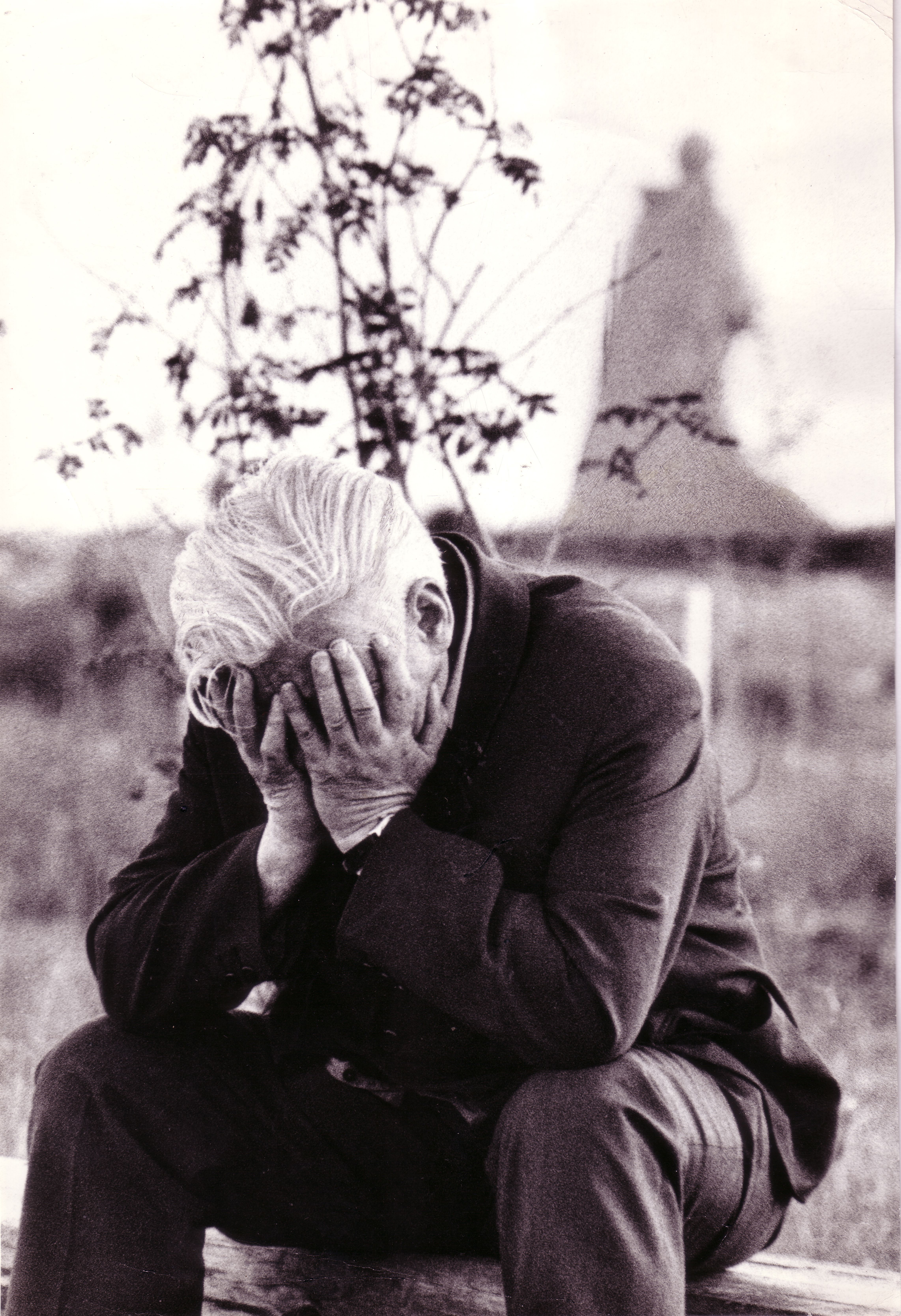 Elderly man sitting outside with face in hands, conveying despair and sadness in a monochrome setting.