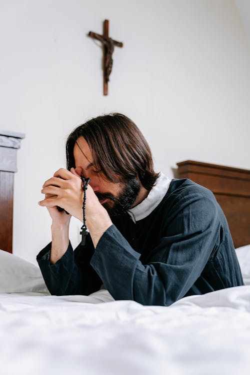 A Man in Black Long Sleeve Shirt Praying with a Rosary