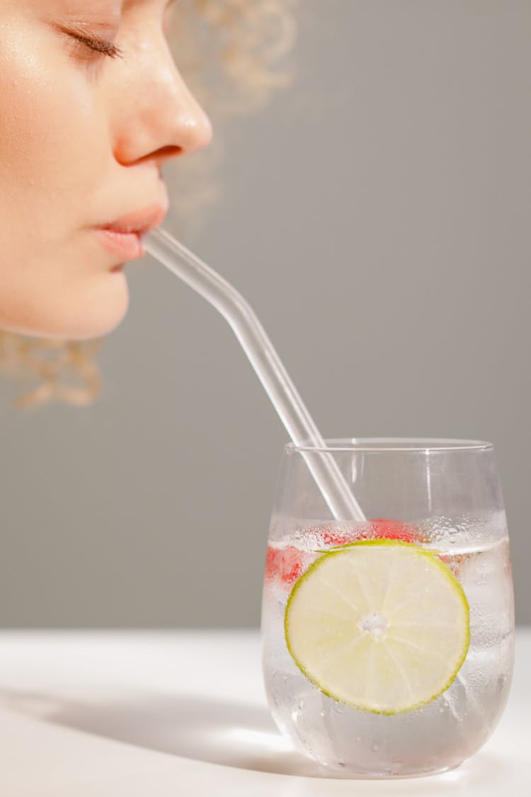 Close-up Of Woman Drinking Water With Lemon Through A Straw 