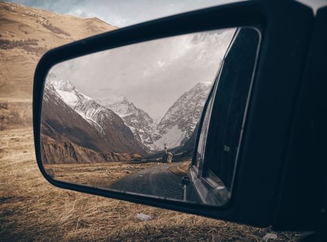 View of a scenic snowy mountain landscape through a car's side mirror, capturing the beauty of nature.