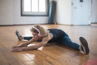 Woman in Blue Tank Top and Blue Denim Jeans Lying on Brown Wooden Floor