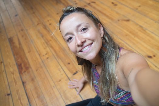 Cheerful woman taking a selfie on a wooden floor indoors.