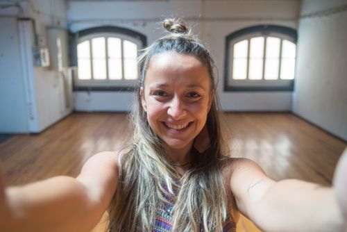 Free Smiling woman with long hair taking a selfie in a bright, empty dance studio with wooden floors. Stock Photo