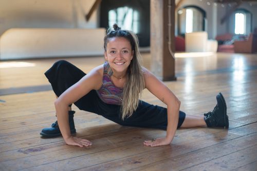Free Smiling woman doing a leg split yoga pose on a wooden floor indoors. Stock Photo
