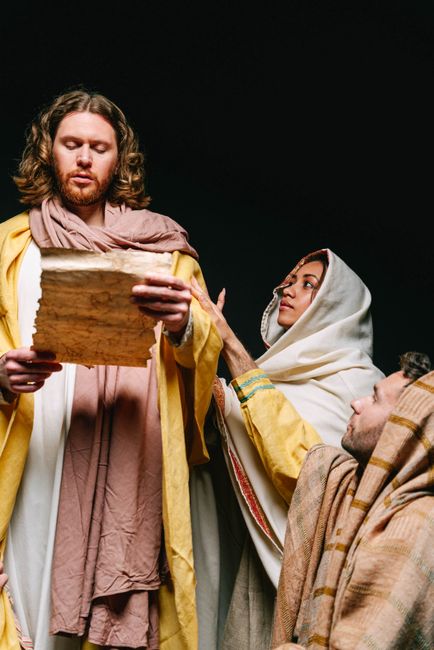 Actors in traditional costumes perform a biblical theatrical scene with a focus on ancient scripture.