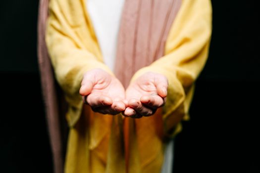 A person in a yellow garment extends open hands in a gesture of offering or invitation.