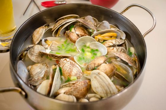 Steel pot of open clams in a pale broth with chopped scallions and garlic