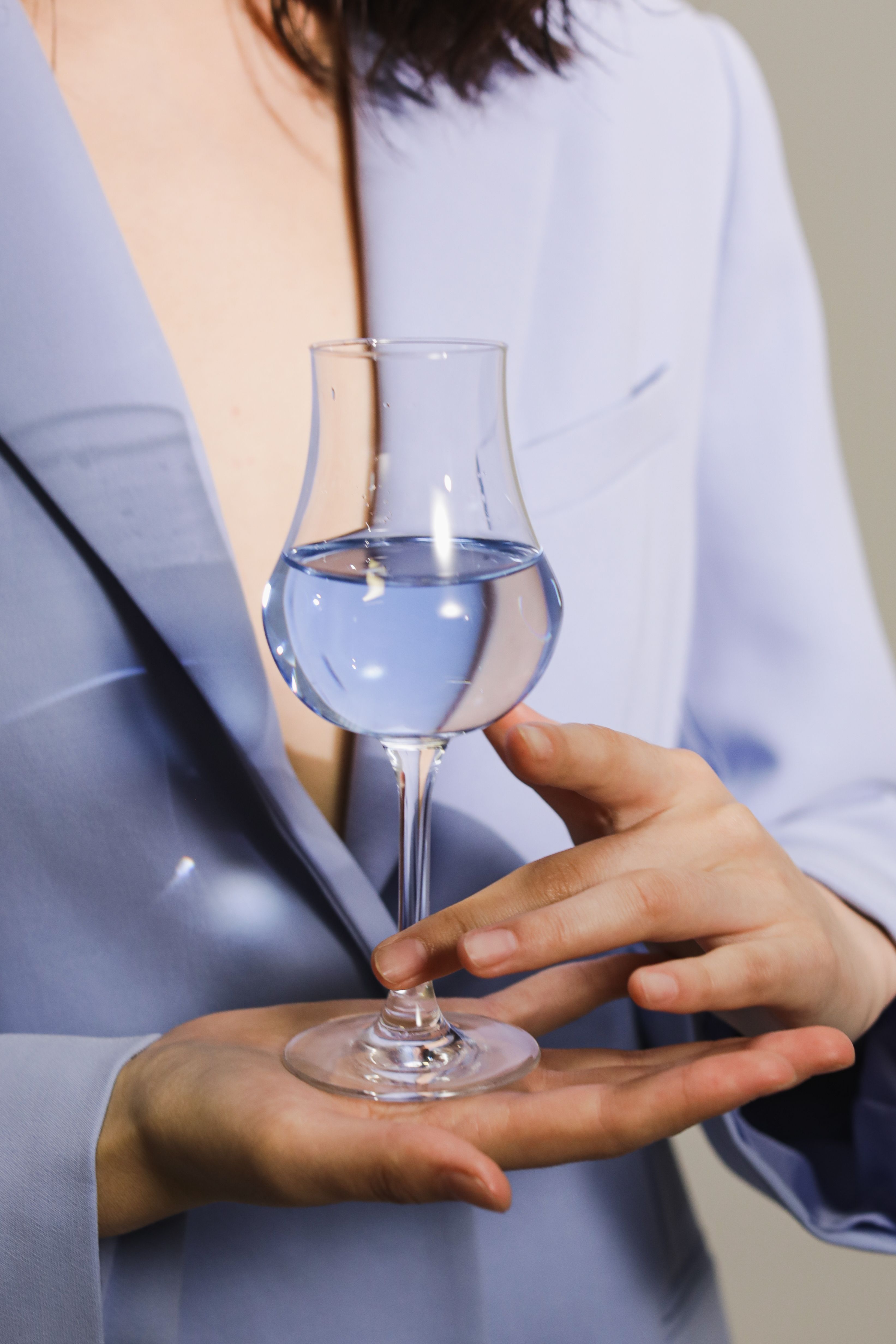 A woman in a stylish blue blazer elegantly holds a glass of water, capturing sophistication.