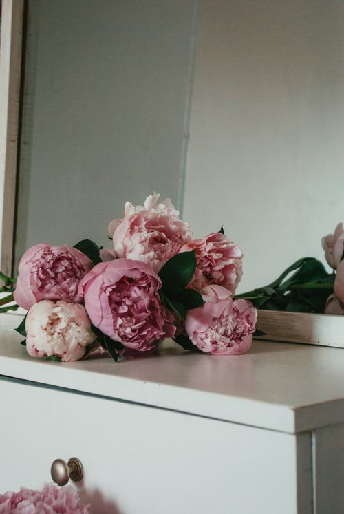 Free A delicate bouquet of pink peonies placed on a white side board with a mirror reflection. Stock Photo