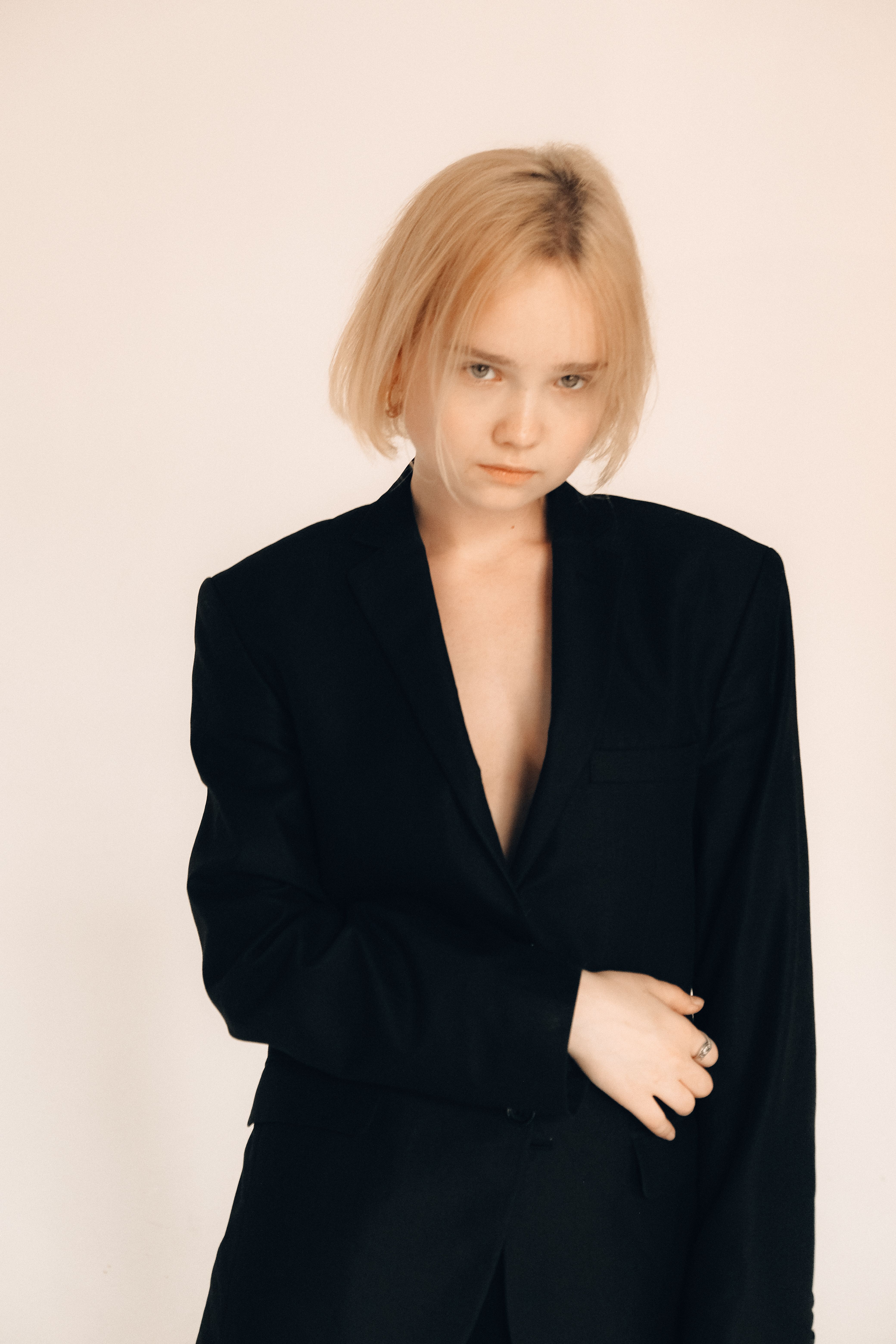 A young woman in a stylish black blazer stands against a neutral background, exuding confidence and elegance.