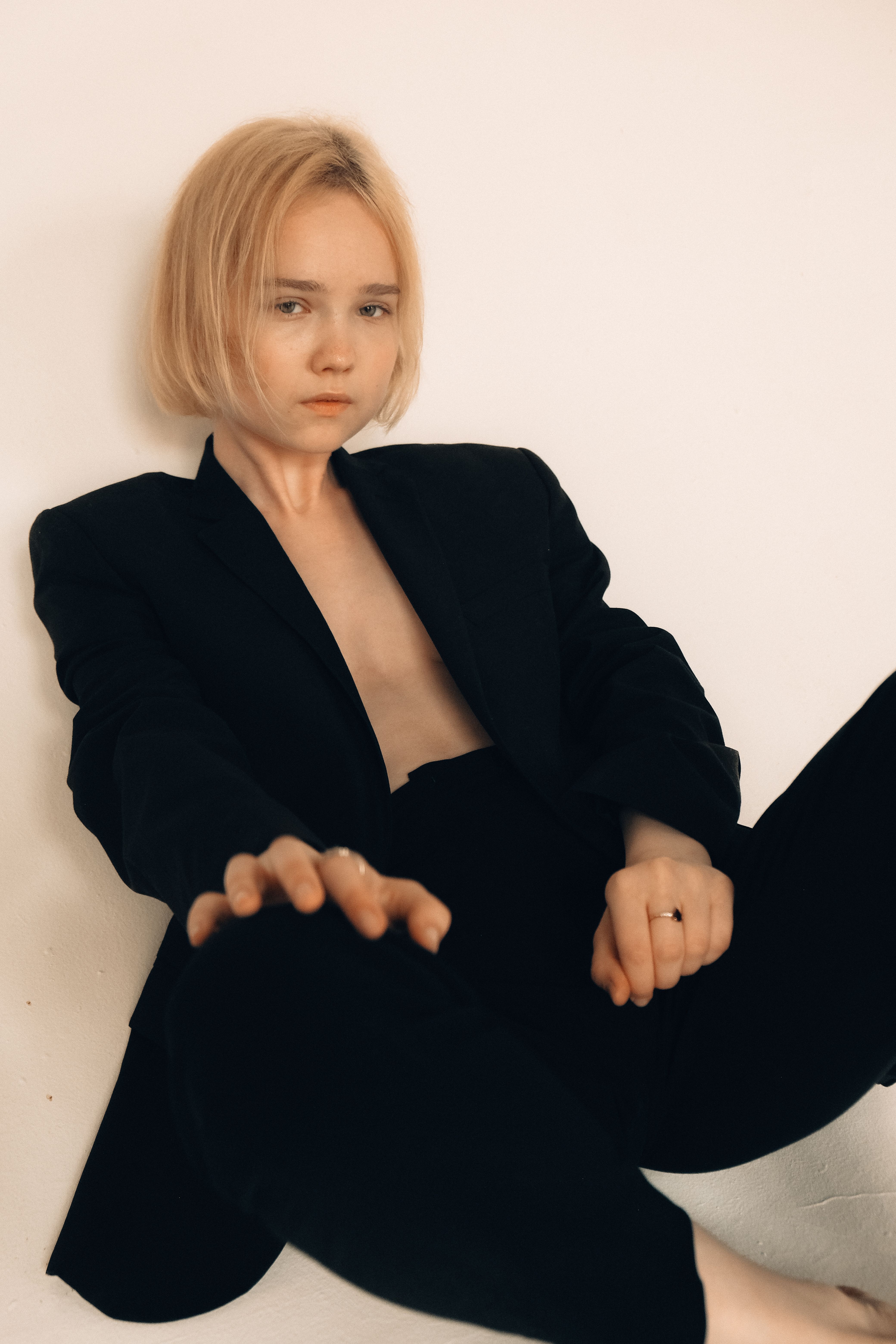 Stylized portrait of a blonde woman posing in a black suit against a minimalist white background.