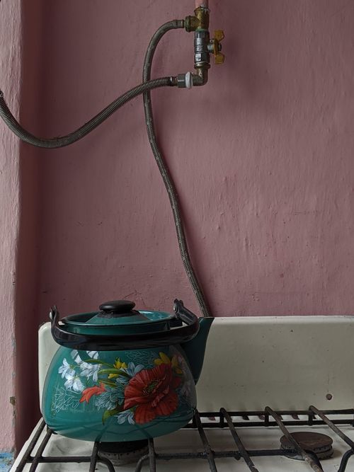 Free A floral design kettle on a retro stove against a pink wall, showcasing vintage kitchen style. Stock Photo