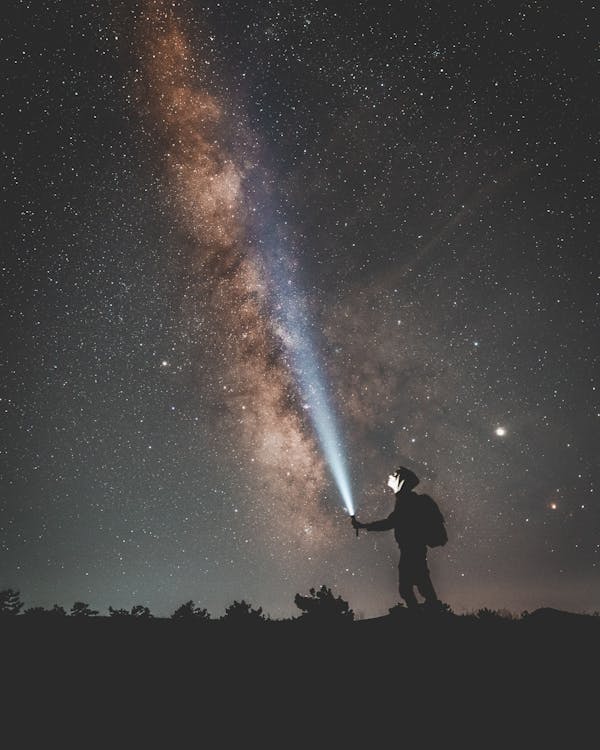 Silhouette of Man Holding a Flashlight Under Starry Night