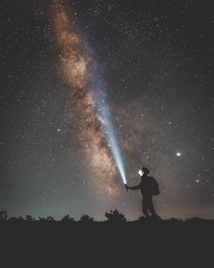 Silhouette Of Man Holding A Flashlight Under Starry Night