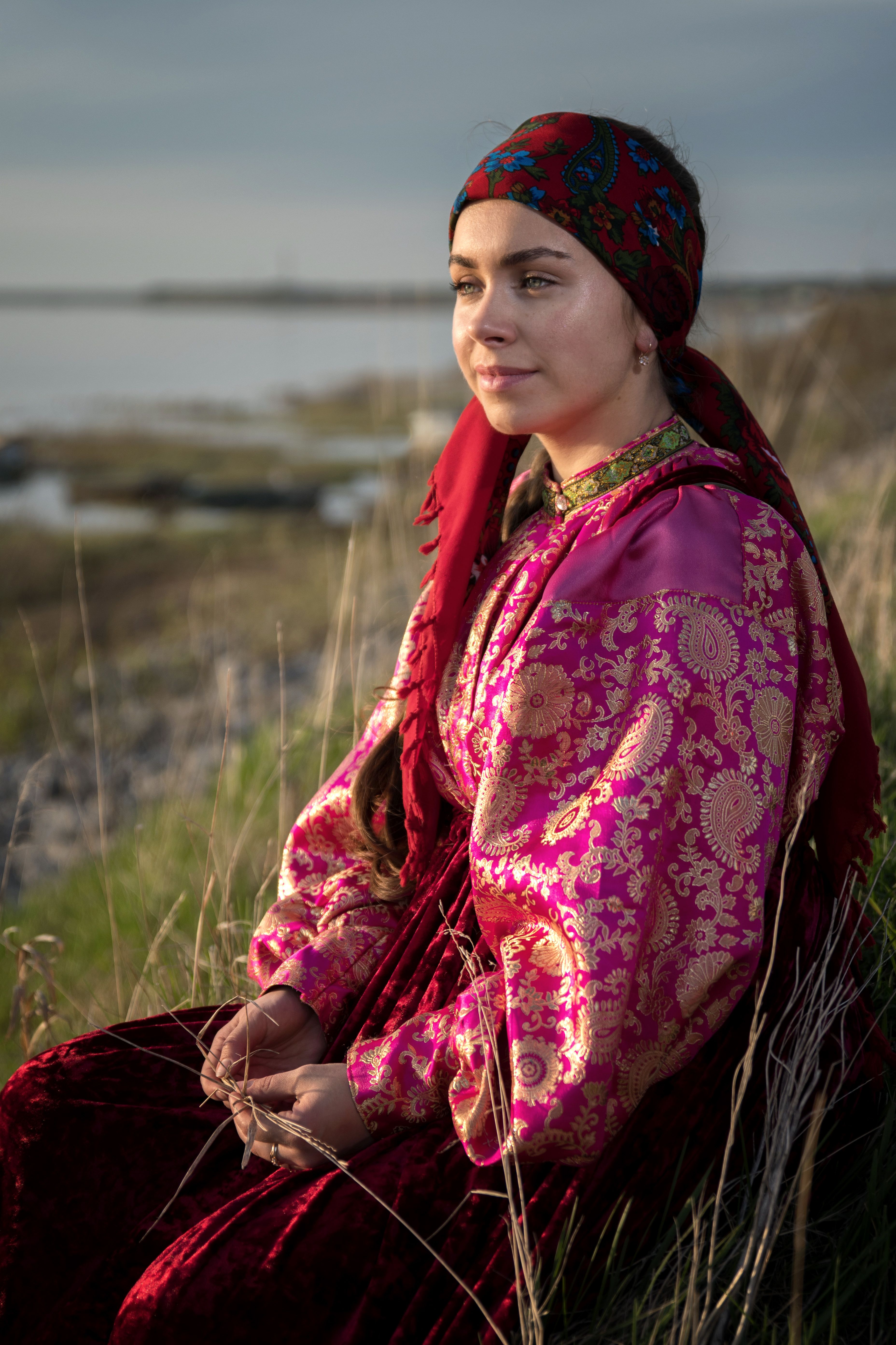 A serene portrait of a woman in traditional attire sitting in nature by the waterfront.