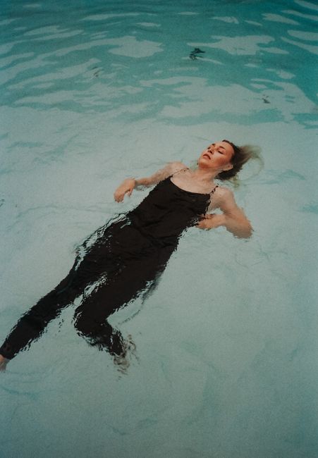 A woman in a black tank top floats peacefully in a pool with eyes closed.