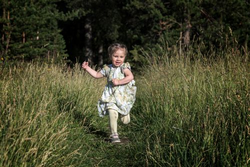 Free A smiling toddler in a floral dress joyfully runs through green grass in a sunny meadow. Stock Photo