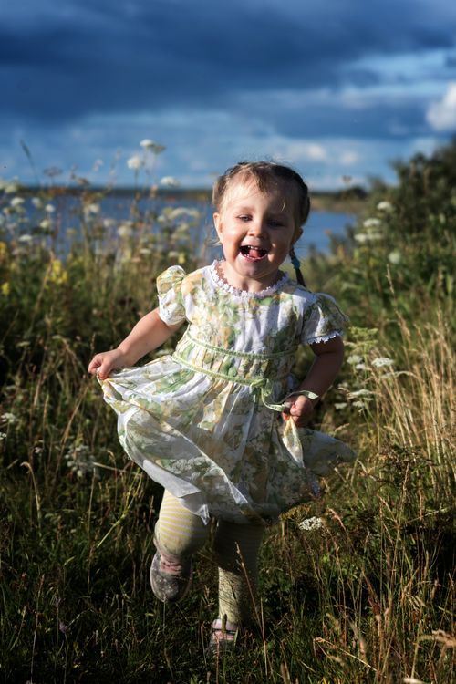 Free A happy child runs through a grassy field under a blue sky, radiating joy and freedom. Stock Photo