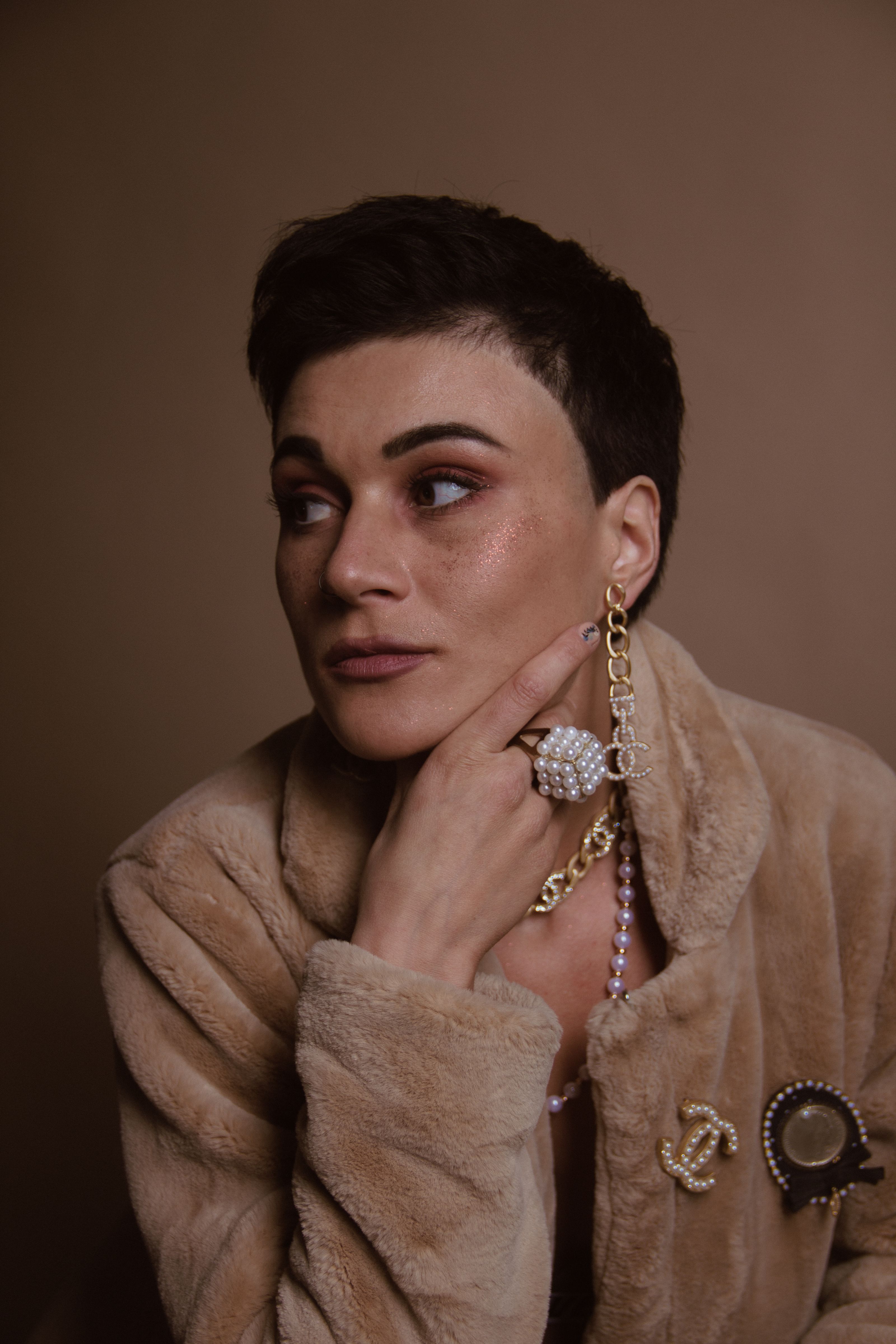 Retrato de uma mulher em casaco de pele adornado com pérolas e broche, evocando elegância clássica.