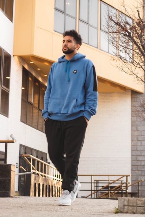 A Man in Blue Hoodie Sweater and Black Pants Walking on the Street