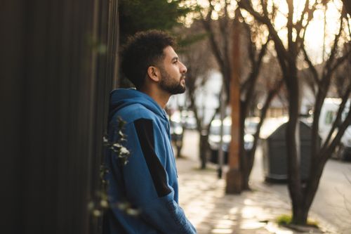 Free Side view of a man in a hoodie leaning against a wall in a city street. Stock Photo