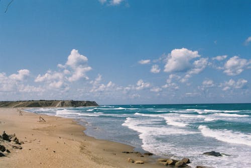 Sea Waves Crashing on Shore Under Blue Sky and White Clouds