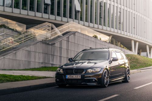 Free Sleek black car parked on the road next to a modern glass facade building with stairs. Stock Photo