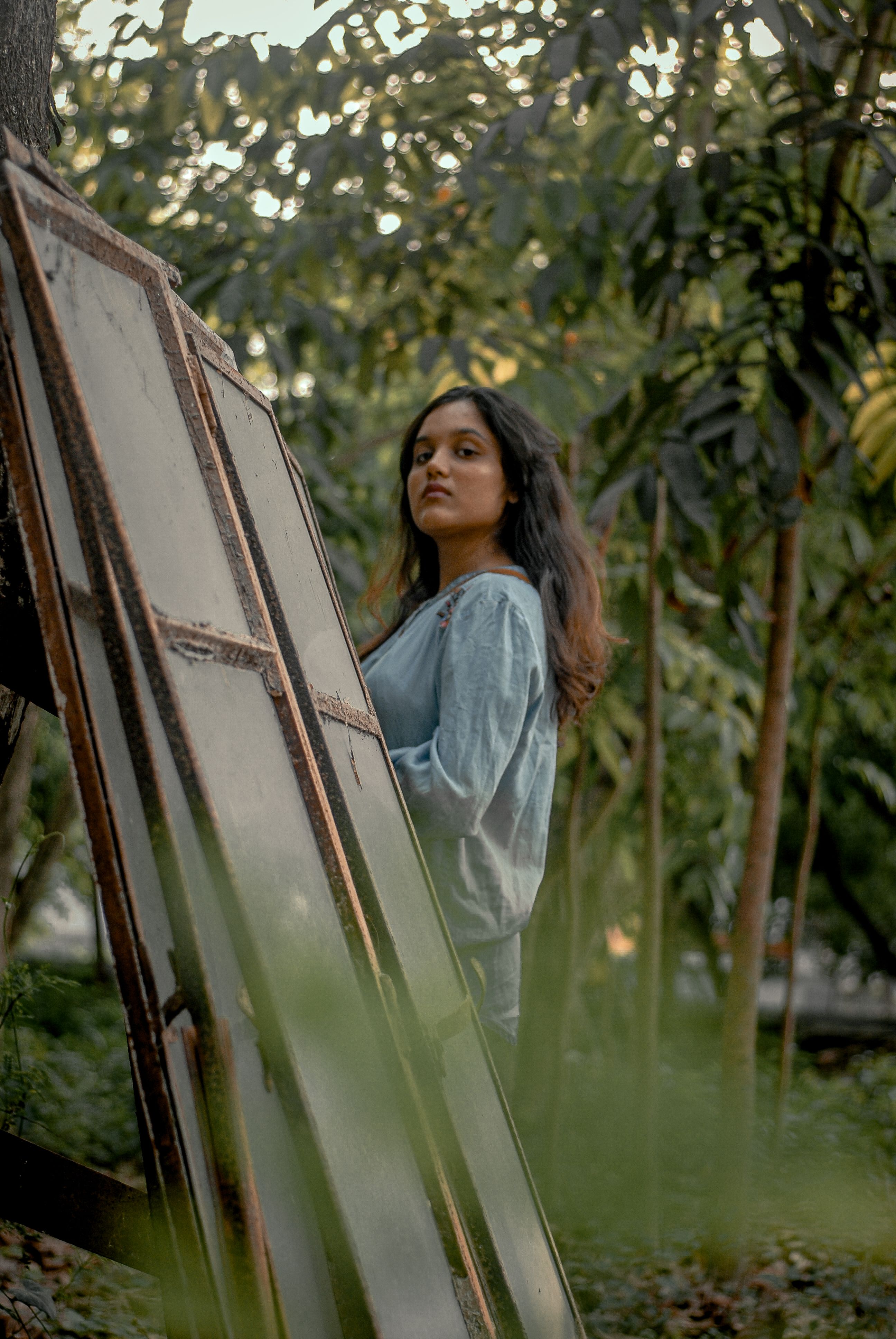 A contemplative portrait of a woman standing in a lush Bangladeshi garden amidst natural surroundings.