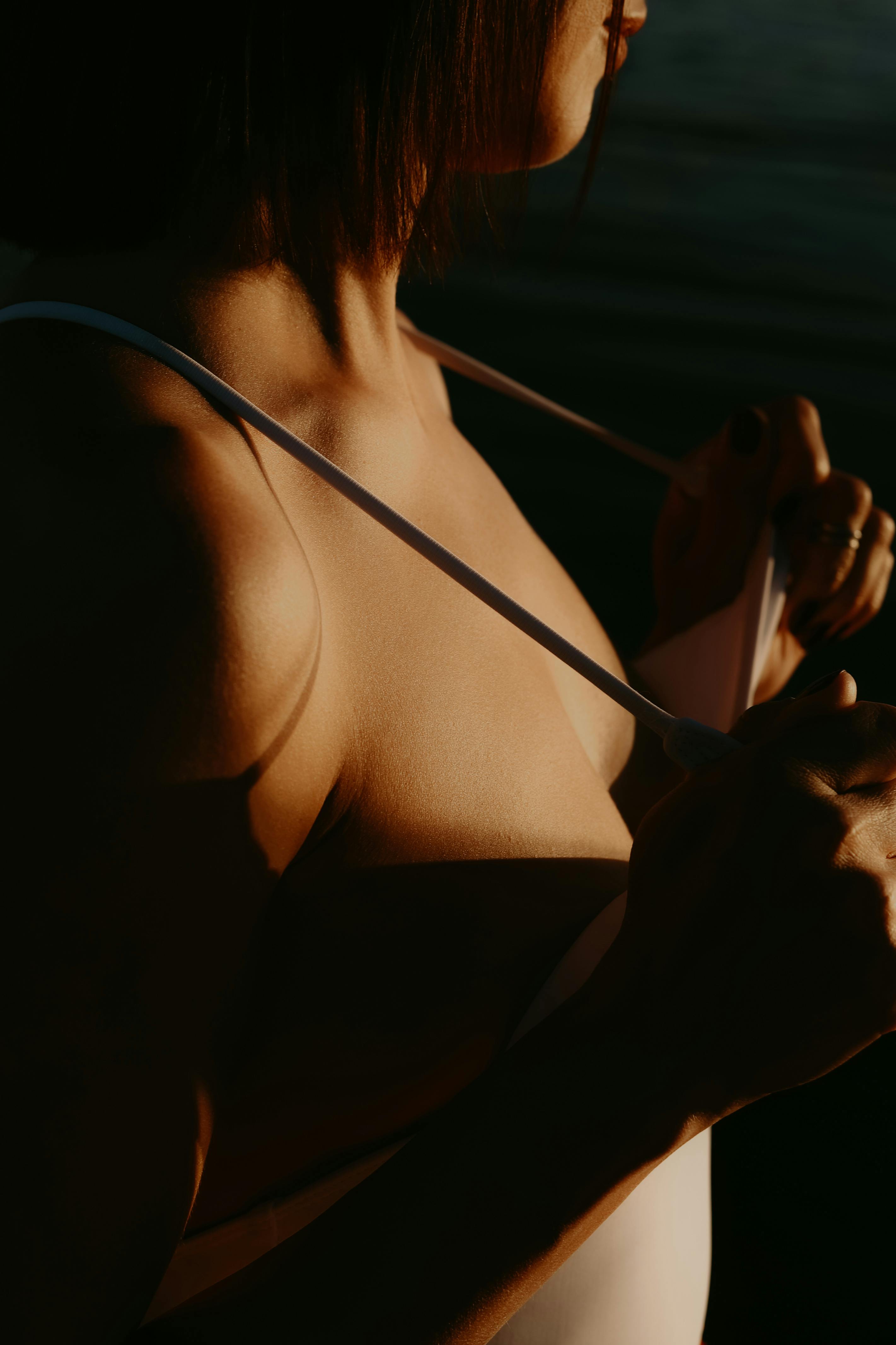 Close-up shot of a woman adjusting her swimwear strap during sunset with dramatic lighting.