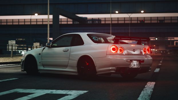 A white Nissan sports car parked under a bridge at night, showcasing luxury and performance.