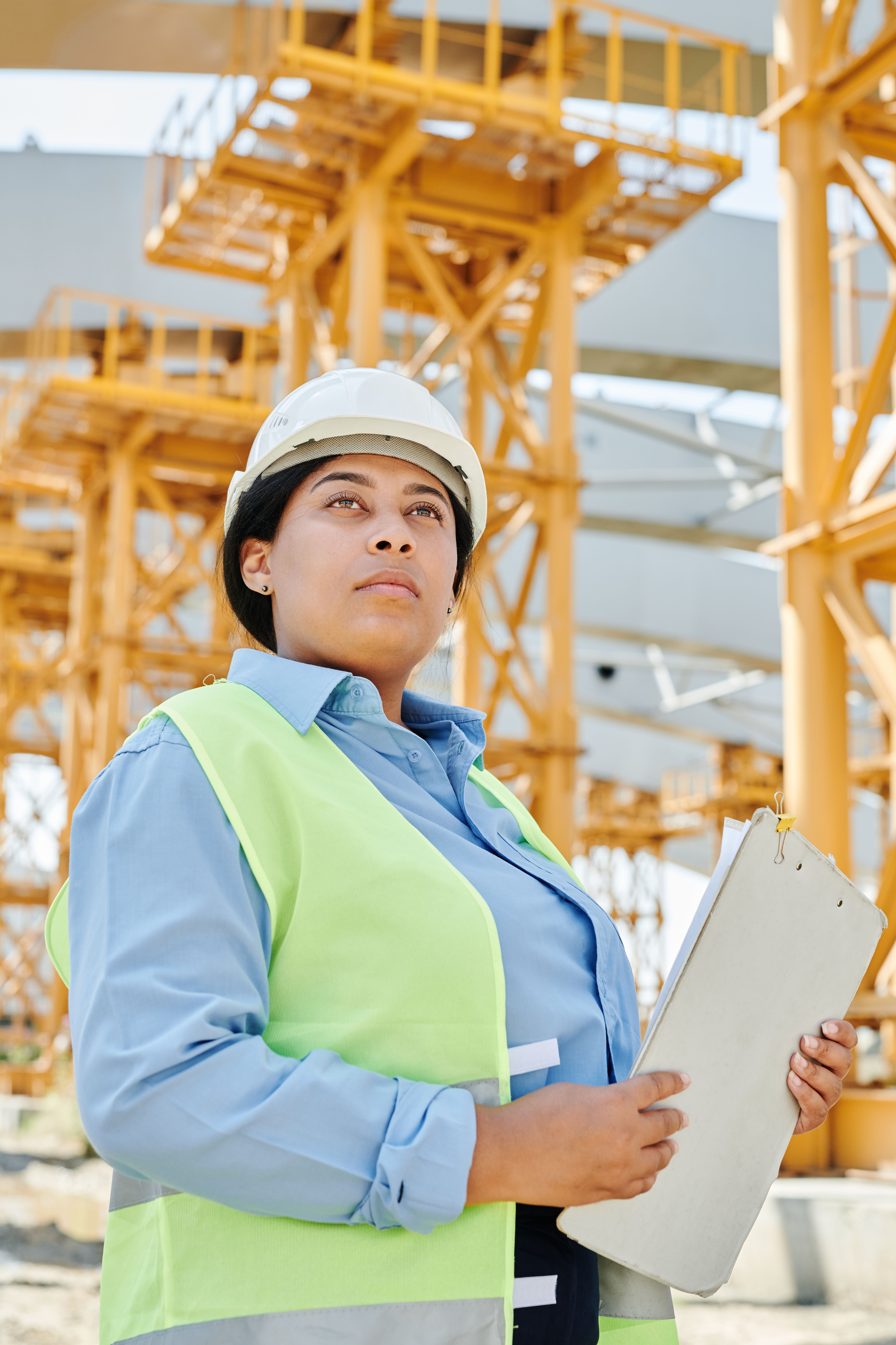 QBCC Licence Application: Eligibility, Steps, Fees & Timeframes 8 Confident female engineer in safe ty gear at a busy construction site, holding a clipboard
