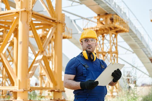 Free Man in Blue Shirt and Yellow Hard Hat Holding White Board Stock Photo