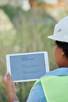 A construction worker examines site plans on a digital tablet outdoors.