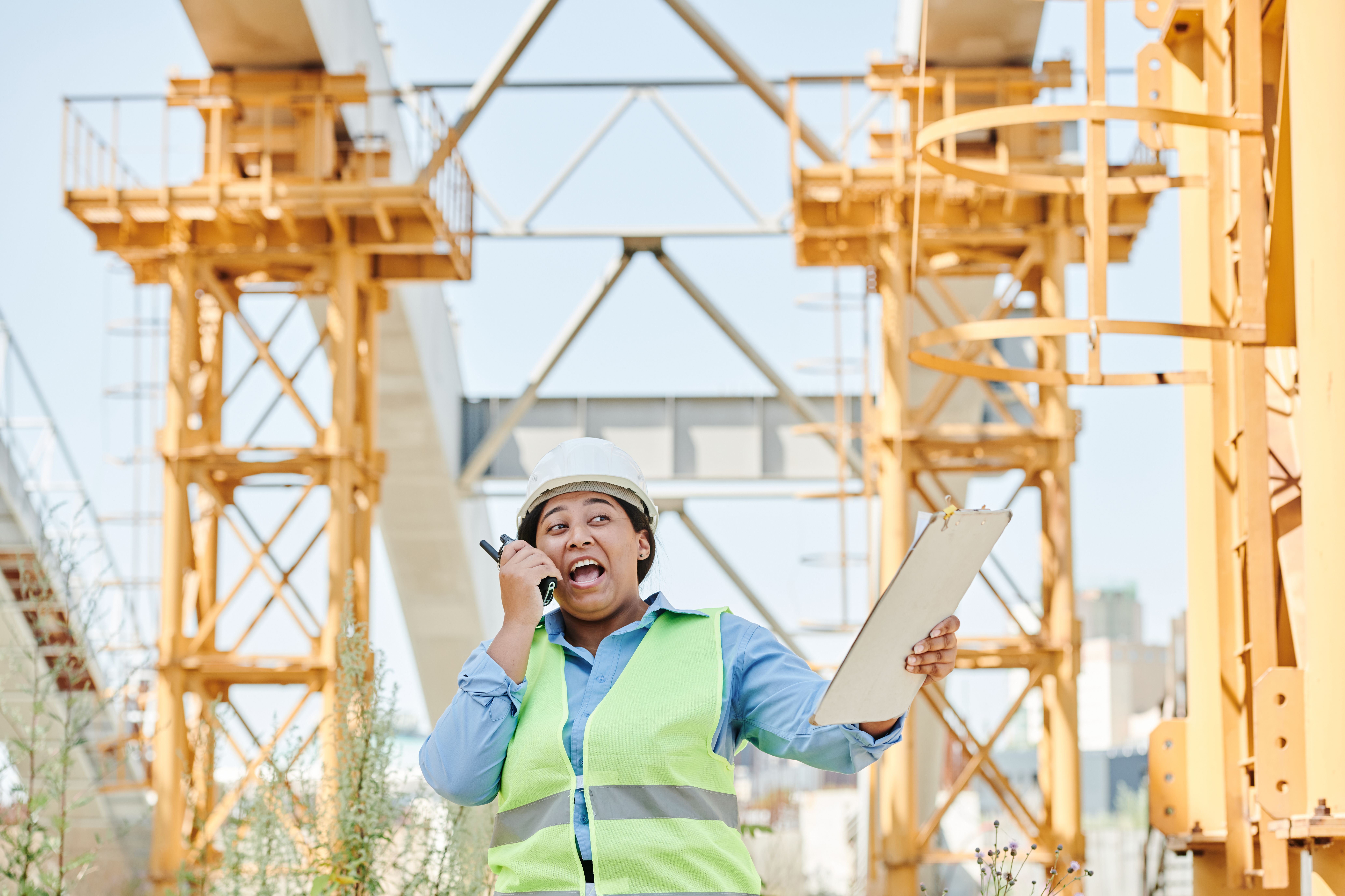 QBCC Licence Application: Eligibility, Steps, Fees & Timeframes 6 Female engineer using walkie-talkie while h olding clipboard on a construction site