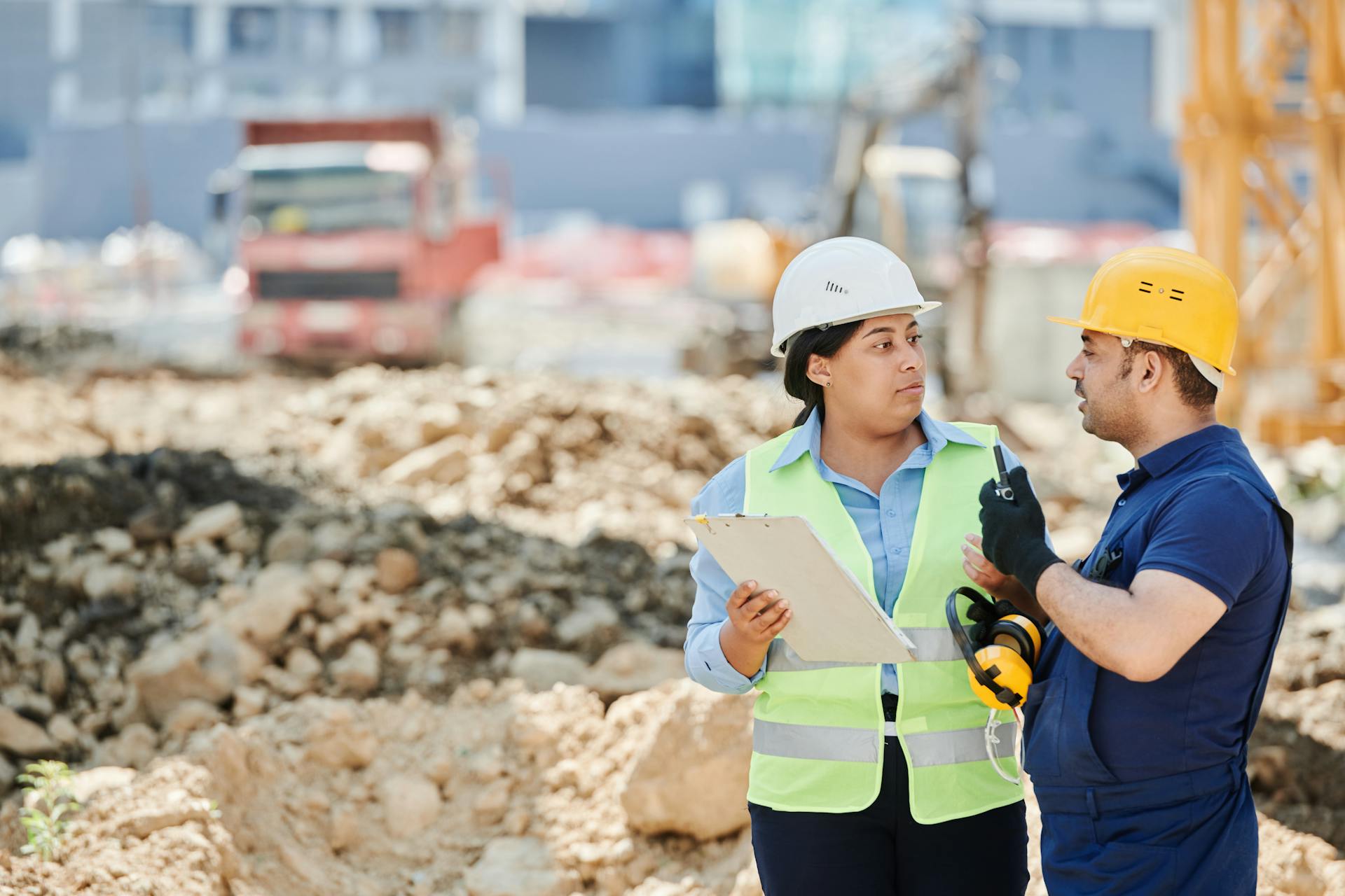 Two construction workers in safety gear discussing plans at a construction site.