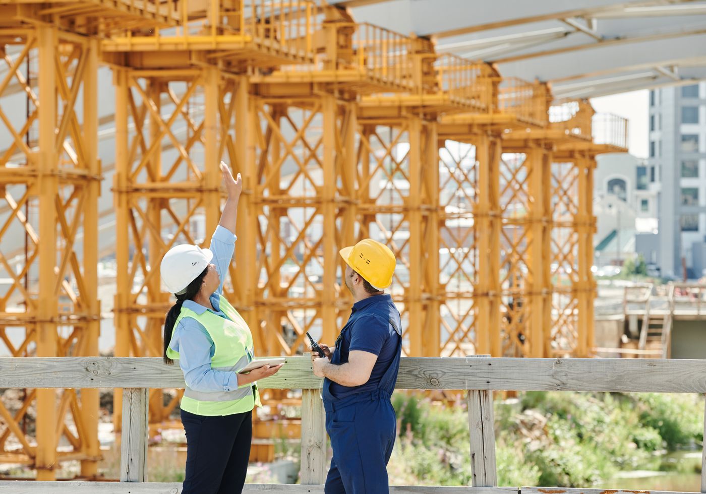 Two workers in hard hats and high visibility vests reviewing a job site