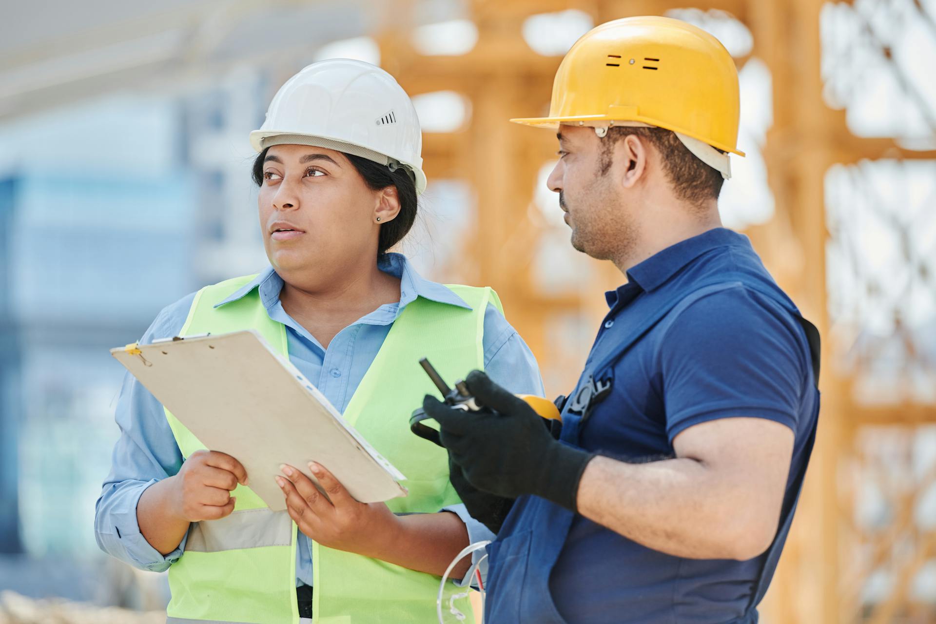 Male and female construction workers converse on a building site wearing hard hats.