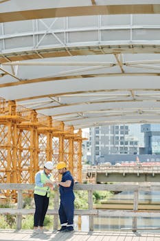 Two engineers discussing plans at an outdoor construction site under a bridge.