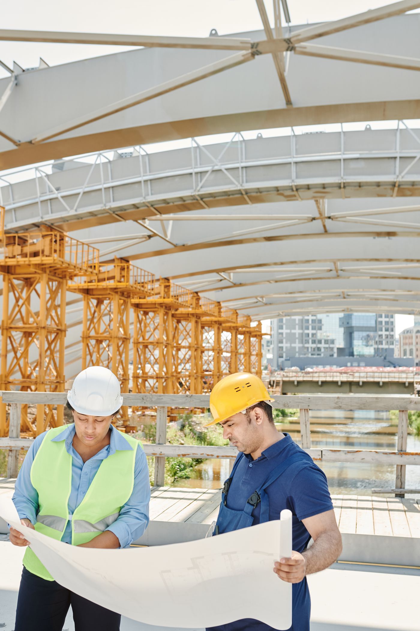 A site engineer and a contractor reviewing a rolled drawing together on a bridge deck under construction