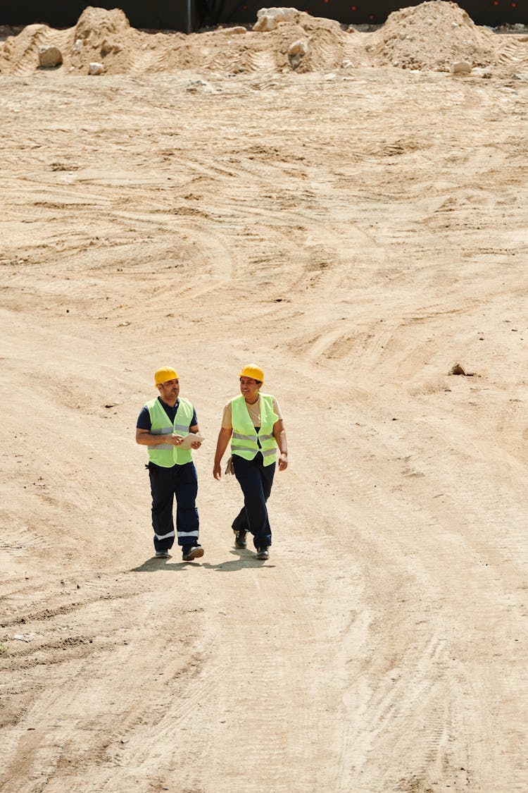 Workers Wearing Safety Vest And Hard Hat Walking On The Dry Ground