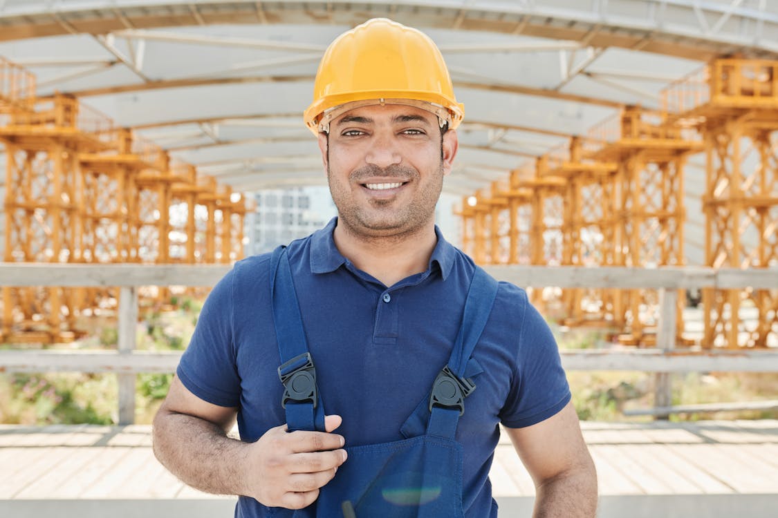 Bauarbeiter in gelber Weste mit Blaupause, lächelnd, sein Kollege im  Hintergrund - Stockfotografie: lizenzfreie Fotos © Dmyrto_Z 384596556
