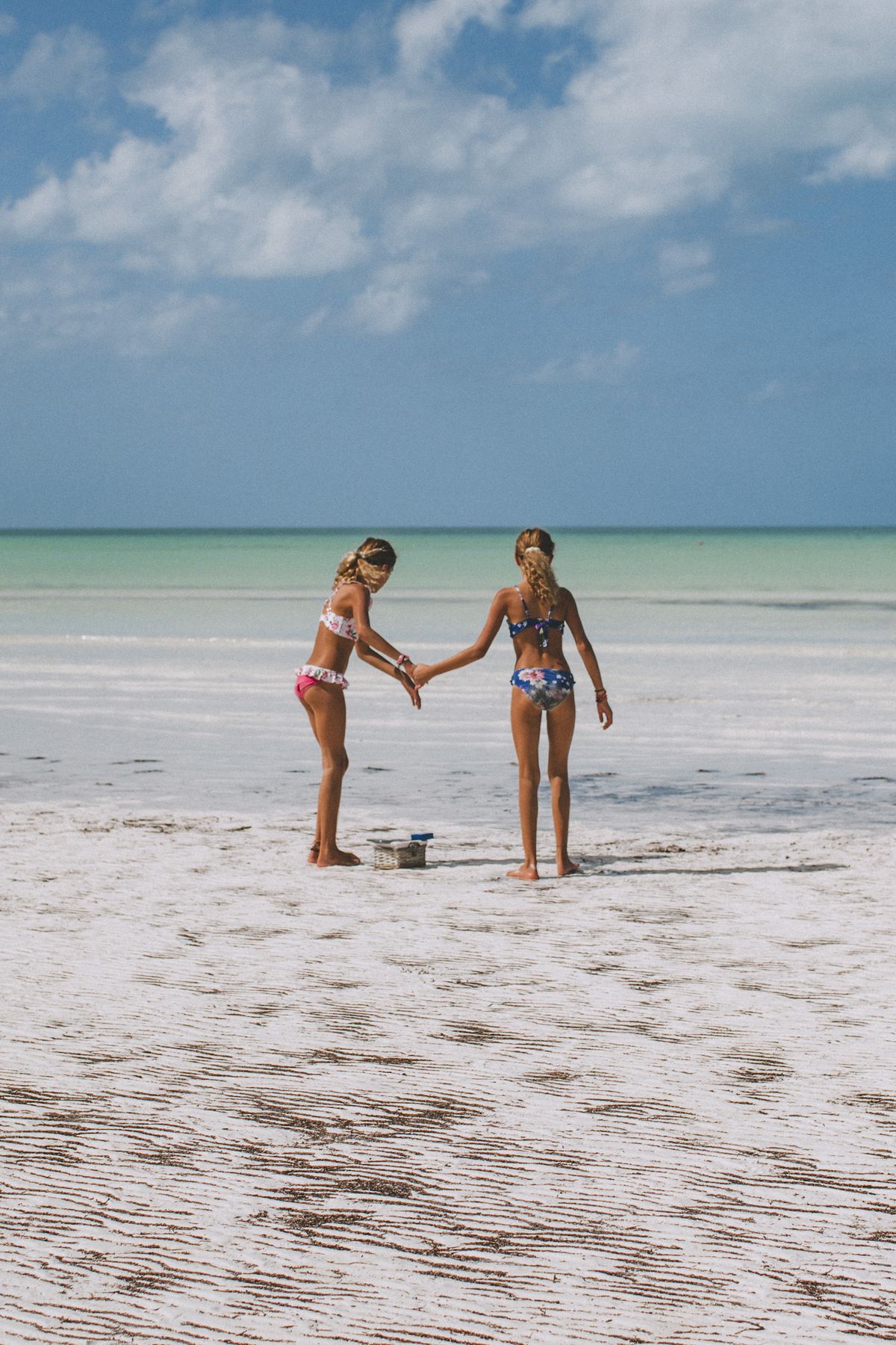 Two girls playing on the sandy beach of Holbox Island, Mexico under a bright blue sky.