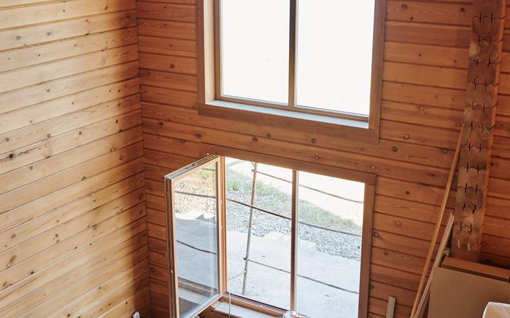 Interior of a rustic wooden cabin with two people resting amid construction materials, capturing a moment of pause.