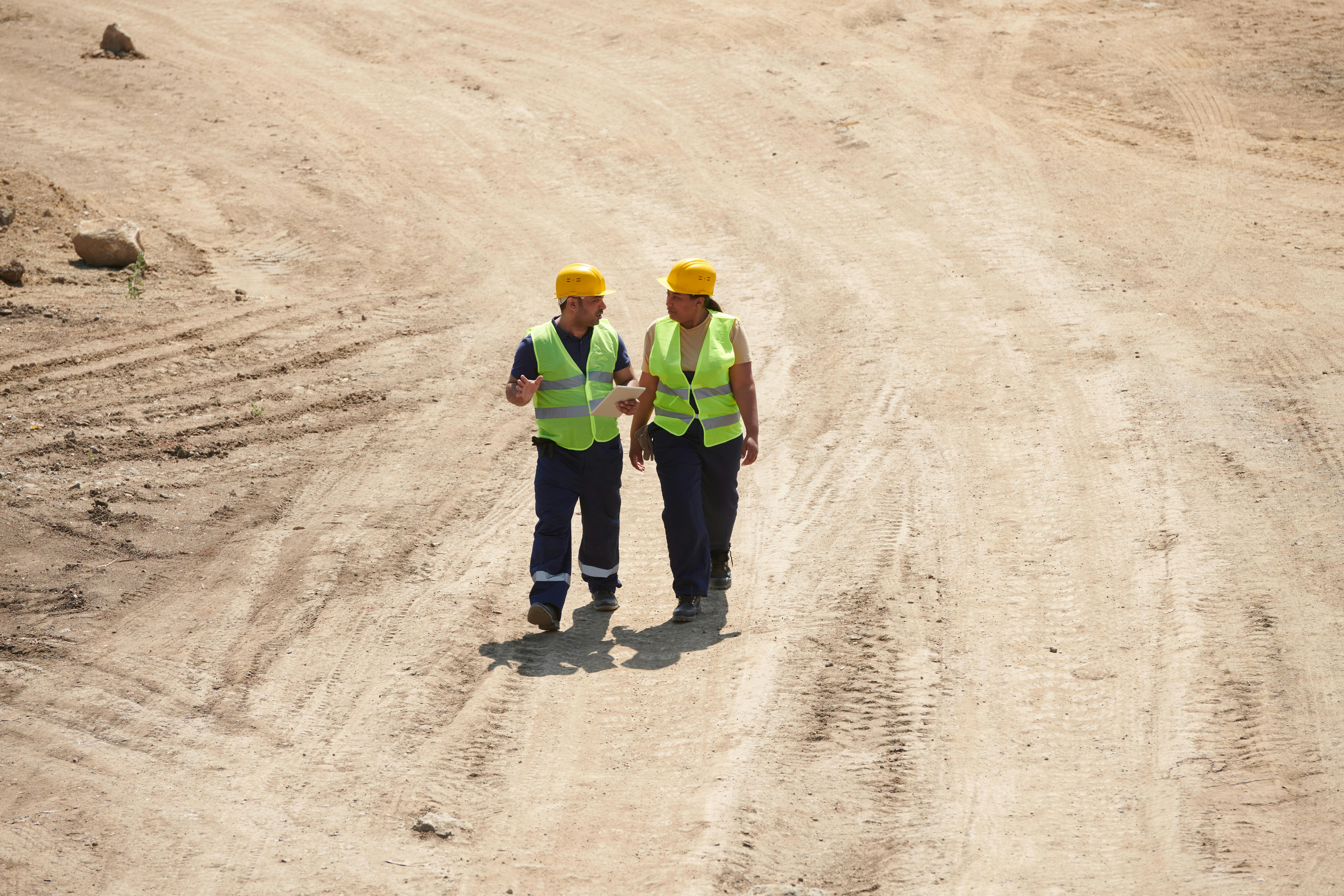 people in safety vest and hat walking on the sand