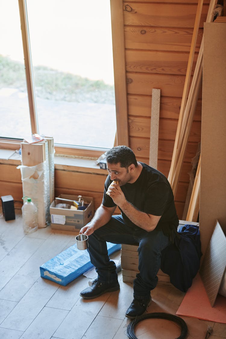 Man In Black Crew Neck T-shirt And Blue Denim Jeans Eating A Sandwich