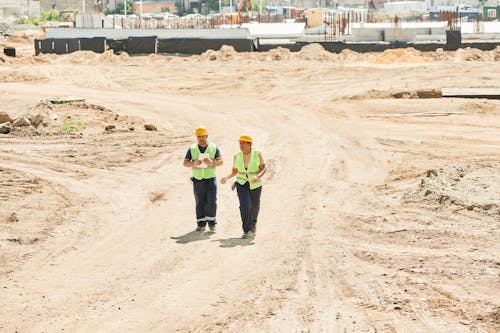 Man and Woman in Helmets and Reflective Vests Walking on a Construction Site